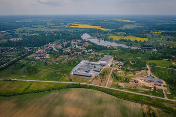 Aerial view of a woodworking factory next to a small village, with beautiful forests and yellow fields in the background