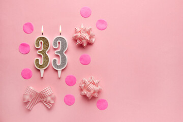 Number 33 on pastel pink background with festive decor. Happy birthday candles. The concept of...