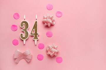 Number 34 on pastel pink background with festive decor. Happy birthday candles. The concept of...