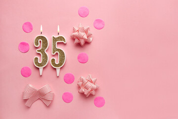 Number 35 on a pastel pink background with festive decor. Happy birthday candles. The concept of...