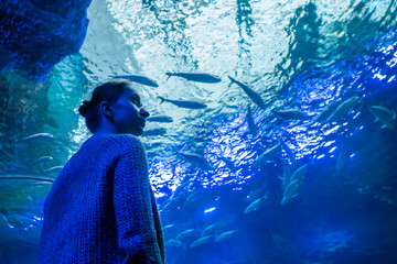 Portrait of woman looking at fish vortex in large public aquarium tank at Oceanarium - low angle...