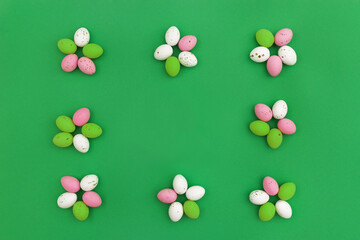 Happy Easter concept. Colorful chocolate eggs arranged in shape of flowers, which form frame on green background. Use for Easter or spring advertising as decorative image for blog. Top view.Copy Space