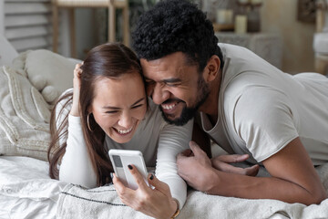 Multiethnic American couple using smartphone lying on bed together