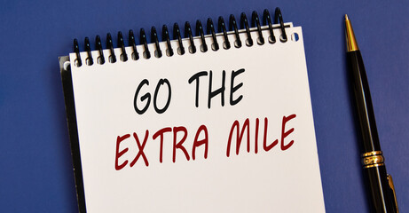 GO THE EXTRA MILE - word in a white notebook on a blue background with a pen