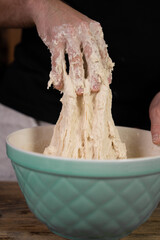 Man is making / kneading homemade pizza dough over blue bowl
