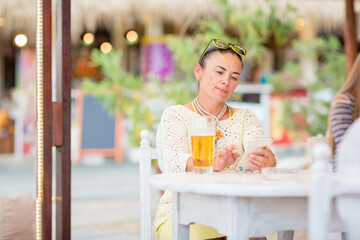 Portrait of beautiful young woman drinking beer at beach cafe and enjoying summer day