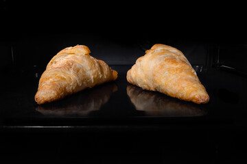 Two baked croissants on tray in electric oven. French cuisine, homemade bakery, breakfast, food, cooking and pastry concept