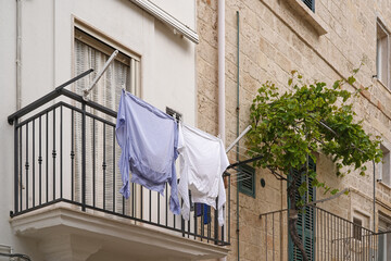 facade of mediterranean style building with balcony with drying laundry and grape vines