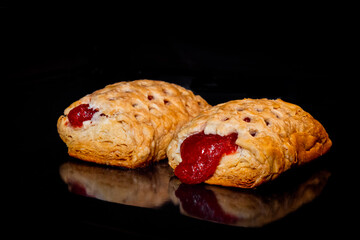 Two baked puff pastry buns with red strawberry jam on tray in electric oven, black background. Homemade bakery, food, cooking and pastry concept