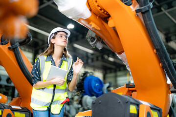 Female technician programs a robot arm with a digital tablet and assembly robot in a factory. Apprentice engineers programming robots in factory.