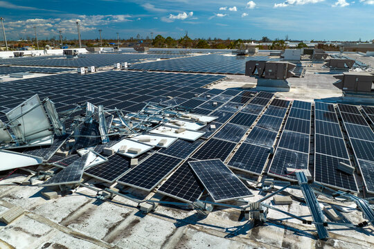 Top view of destroyed by hurricane Ian photovoltaic solar panels mounted on industrial building roof for producing green ecological electricity. Consequences of natural disaster in Florida
