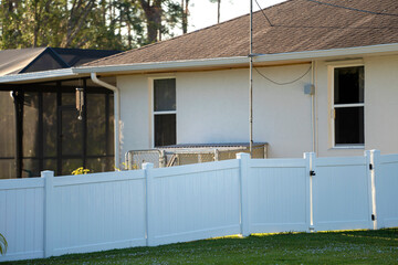White vinyl picket fence on green lawn surrounding property grounds for backyard protection and...