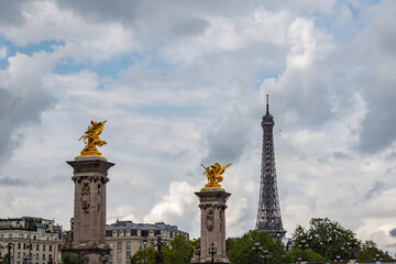 Fototapeta premium Renowned gilt bronze surmounted pylon of the Alexandre III bridge with the Eiffel tower in background from the Seine, in Paris, France