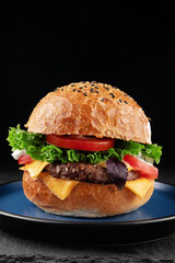 Hamburger with cheese, lettuce and tomato on black background.