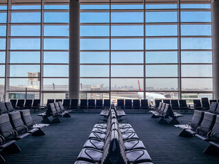 Empty chairs in the departure hall at airport , with the control tower and an airplane taking off...