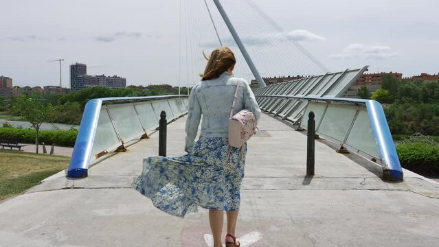 Woman strolling over a modern bridge on a windy day in the city, Zaragoza.