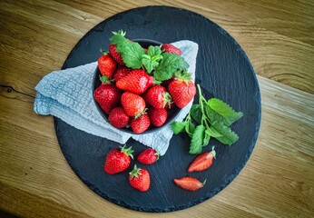 Schale frische Erdbeeren auf schwarzer Schieferplatte mit grüner Minze serviert