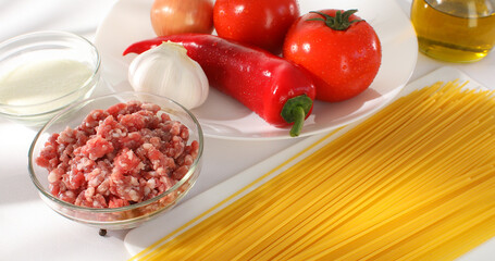 ingredients for spaghetti bolognese. pasta with minced meat and fresh vegetables on the table. tomatoes, paprika, onion, garlic and olive oil. illustration for a traditional dish recipe.
