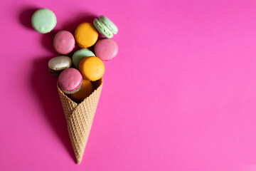 A colourful macarons or French macaroons in an ice cream waffle cone on a bright pink background. Top view, copy space