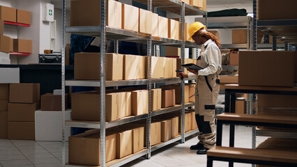 Young woman scanning barcodes on packages to work on stock logistics, using scanner and examining cargo for shipment. Female employee looking at delivery boxes on shelves for distribution.