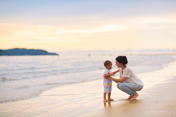 Mother and baby on tropical beach at sunset.