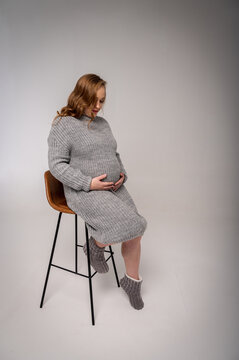 full length portrait of a pregnant woman resting sitting on a chair on a light background, excited in anticipation, full photo, space for text