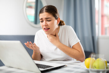 Portrait of young woman suffering from sore throat using laptop having video conference with doctor...