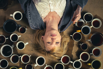 Fototapeta na wymiar The concept of a deadline, the need to stay cheerful. Woman surrounded by many cups of coffee.