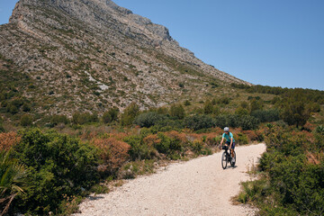 Fit female cyclist riding dirt trails on a gravel bike.Gravel road in mountains.Alicante region of Spain.