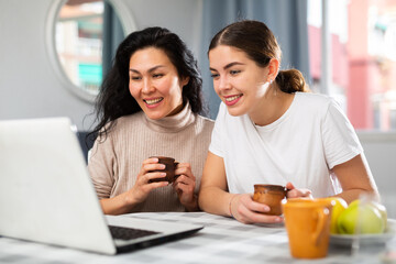 Positive Asian and European women having video call conversation at home.