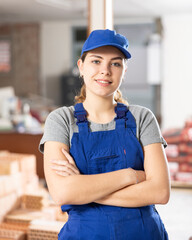 Positive smiling young female foreman in blue coveralls posing at indoor building site