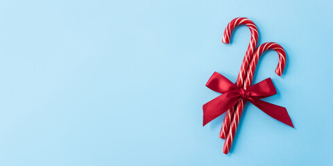 Candy canes are decorated with red bow on blue background. Minimal Christmas banner. Selective focus, copy space