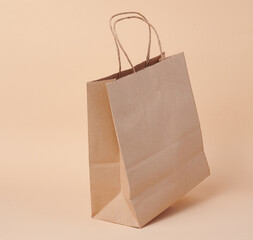 Disposable brown kraft paper bag with handles on beige background, eco packaging, zero waste