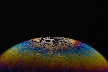 Rainbow reflection in soap bubble on black background. Planet