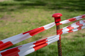 Warning tape with red and white diagonal stripes. Warn stop tape on a metal bar encloses the lawn....