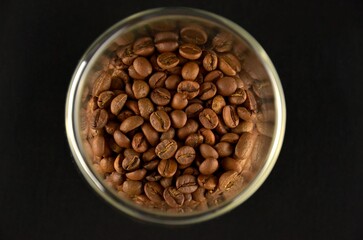 A bunch of coffee beans in a glass jar on a black background
