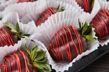 Multiple dark chocolate-covered strawberries with green tuffs and red frosting drizzle on black tray
