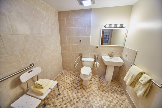 Retirement home handicap bathroom, seating, railing next to toilet wheelchair and walker access
