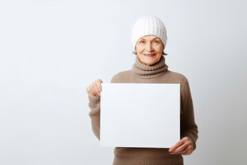 Senior woman in winter clothes holding a white sheet of paper on a white background