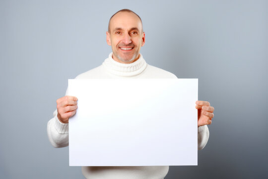 Portrait of a smiling man holding blank sheet of paper on grey background