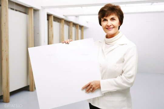 Mature businesswoman holding white sheet of paper in office. Focus on woman
