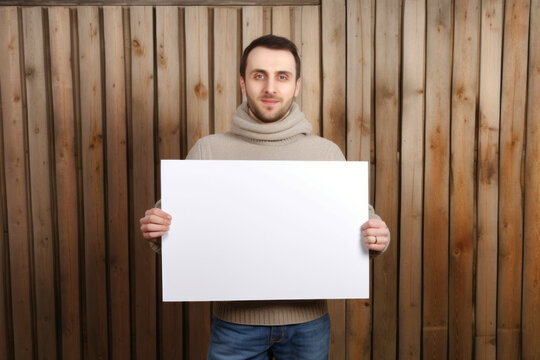 Handsome young man holding blank sheet of paper on wooden background