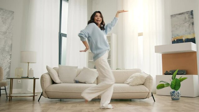 Slow Motion of happy funny young woman dancing at home. Multi ethnical hispanic girl having fun celebrating with funny dance moves, enjoying freedom on weekend morning, 4k footage stylish living room
