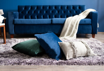 a blue couch with pillows is on the carpet next to a white thrower