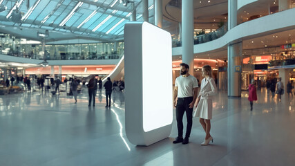 a couple man and a woman standing in-front of a big white mockup blank screen at a shopping mall or center - Generative AI