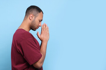 African American man with clasped hands praying to God on light blue background. Space for text