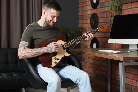 Smiling hipster man playing guitar in stylish room