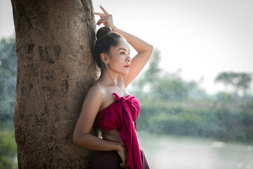 Portrait of beautiful young woman wearing traditional Thai dress in unique cultural dress posing with nature in the background