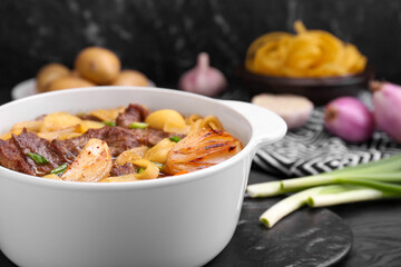 Pot of delicious vegetable soup with meat, noodles and ingredients on black wooden table, closeup. Space for text