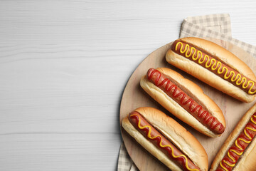 Fresh delicious hot dogs with sauces on white wooden table, top view. Space for text